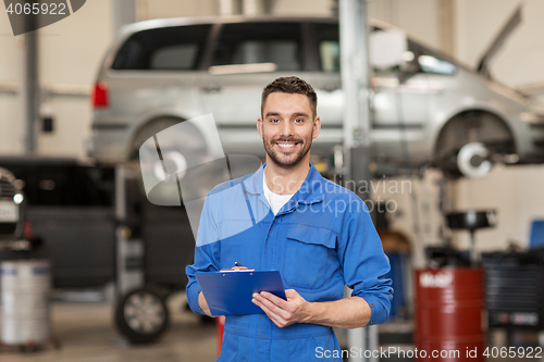 Image of happy mechanic man with clipboard at car workshop