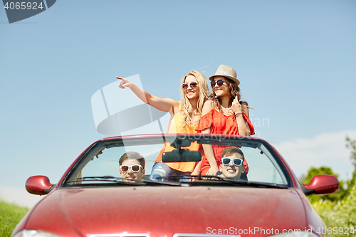 Image of happy friends driving in cabriolet car at country