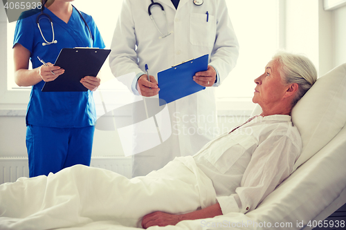 Image of doctor and nurse visiting senior woman at hospital