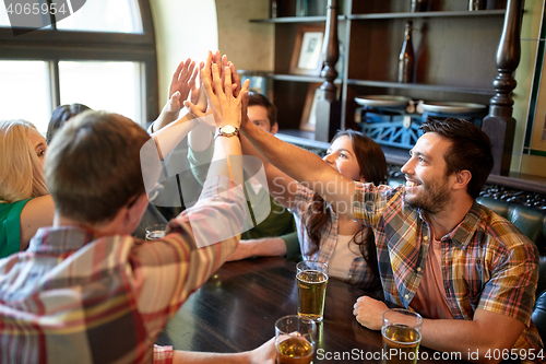 Image of friends with beer making high five at bar or pub