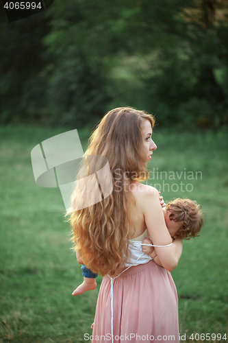 Image of Young beautiful mother hugging her little toddler son against green grass. Happy woman with her baby boy on a summer sunny day. Family walking on the meadow.