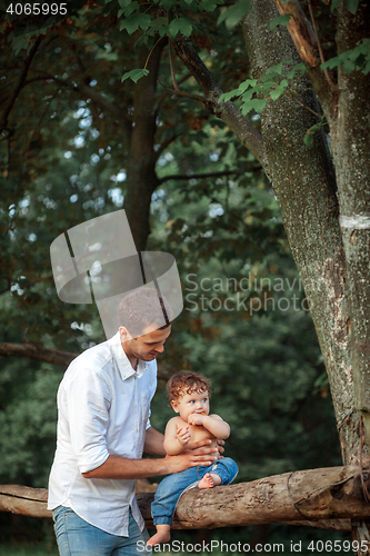 Image of Young beautiful father and little toddler son against green trees