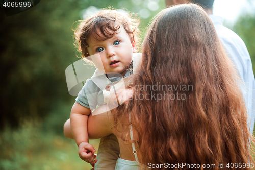 Image of Young beautiful mother hugging her little toddler son against green grass. Happy woman with her baby boy on a summer sunny day. Family walking on the meadow.