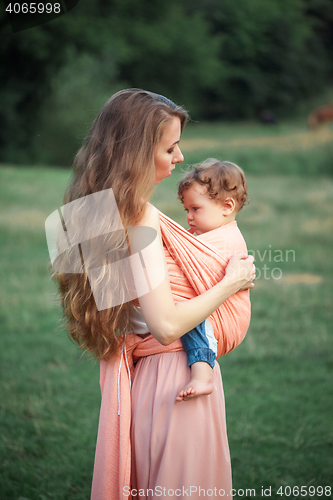 Image of Young beautiful mother hugging her little toddler son against green grass. Happy woman with her baby boy on a summer sunny day. Family walking on the meadow.