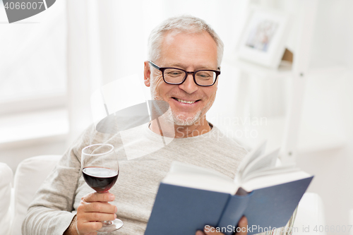 Image of happy senior man drinking wine and reading book