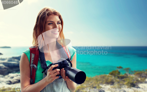 Image of happy woman with backpack and camera over seashore