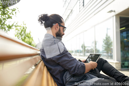 Image of man with tablet pc sitting on city street bench