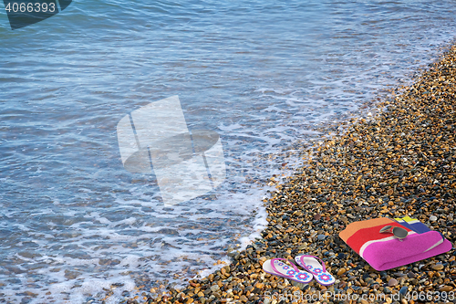 Image of Beach shoes and a towel on the beach.