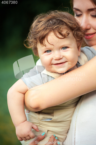 Image of Young beautiful mother hugging her little toddler son against green grass. Happy woman with her baby boy on a summer sunny day. Family walking on the meadow.