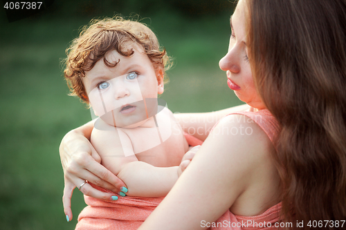 Image of Young beautiful mother hugging her little toddler son against green grass. Happy woman with her baby boy on a summer sunny day. Family walking on the meadow.