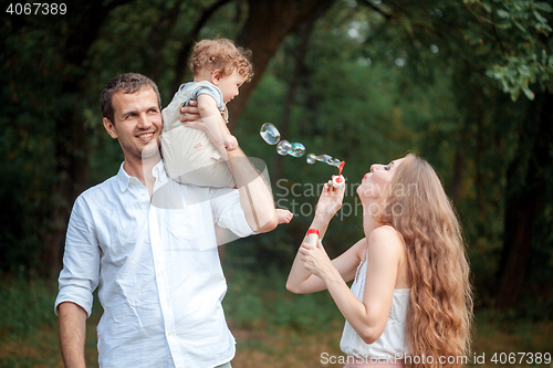 Image of Young beautiful father, mother and little toddler son against green trees