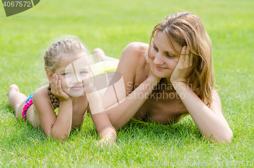Image of Young mother lying on green grass and looking at his five-year daughter who is lying near