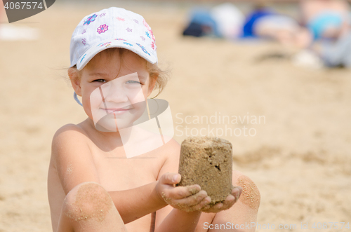 Image of Girl keeps hands on the turret of sand sitting on a river beach