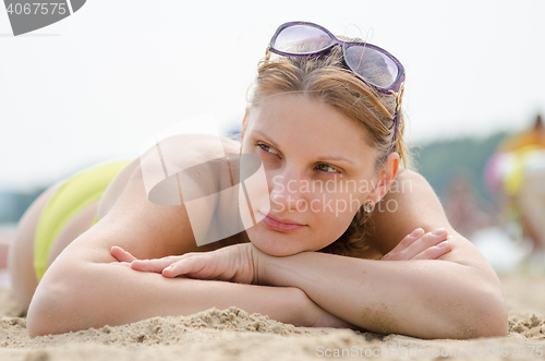 Image of Sad young girl lying on sandy beach and looking to the side