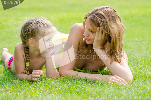 Image of Young mother and five year old daughter lying on green grass and looking at each other