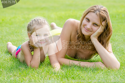 Image of Young mother and five year old daughter lying on green grass and looking to the frame