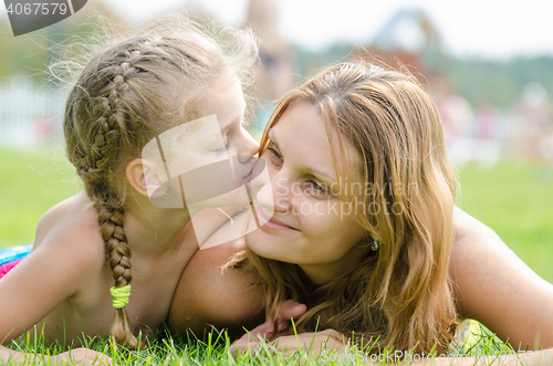 Image of The five-year daughter kissing her mother lying on green grass lawn