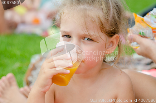 Image of Girl drinking fruit juice from a plastic disposable cup and looked into the frame