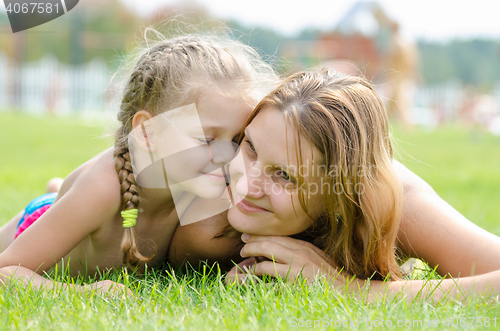 Image of Five-year cute daughter pressed her face to the mother\'s face on a green grass lawn