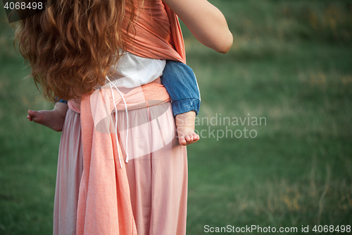 Image of Young beautiful mother hugging her little toddler son against green grass. Happy woman with her baby boy on a summer sunny day. Family walking on the meadow.