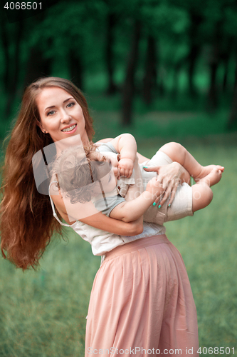 Image of Young beautiful mother hugging her little toddler son against green grass. Happy woman with her baby boy on a summer sunny day. Family walking on the meadow.