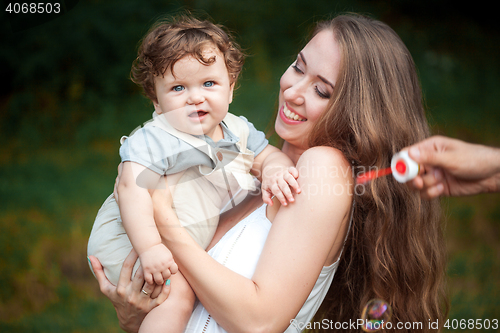 Image of Young beautiful mother hugging her little toddler son against green grass. Happy woman with her baby boy on a summer sunny day. Family walking on the meadow.