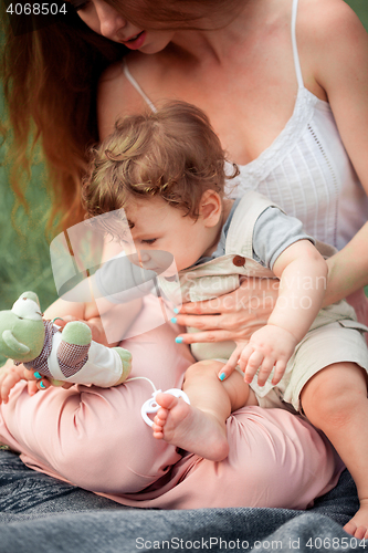 Image of Young beautiful mother sitting with her little son against green grass. Happy woman with her baby boy on a summer sunny day. Family walking on the meadow.