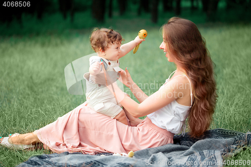 Image of Young beautiful mother sitting with her little son against green grass. Happy woman with her baby boy on a summer sunny day. Family walking on the meadow.