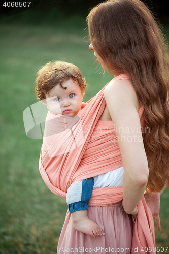 Image of Young beautiful mother hugging her little toddler son against green grass. Happy woman with her baby boy on a summer sunny day. Family walking on the meadow.