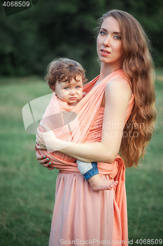 Image of Young beautiful mother hugging her little toddler son against green grass. Happy woman with her baby boy on a summer sunny day. Family walking on the meadow.