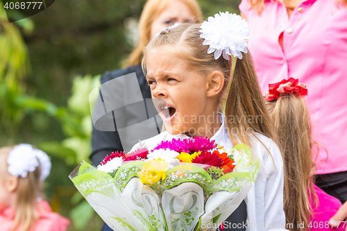 Image of First grader with a bouquet of flowers yawns at school in a crowd