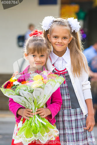 Image of Portrait of two girls in school September 1 - the first-grader and her younger sister with a bouquet in hands