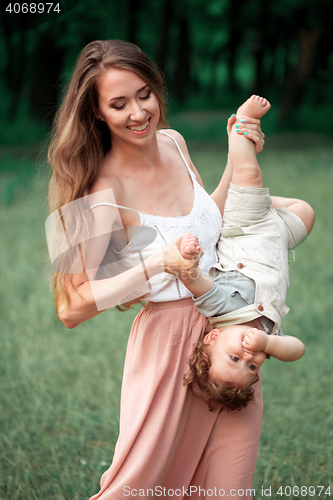 Image of Young beautiful mother hugging her little toddler son against green grass. Happy woman with her baby boy on a summer sunny day. Family walking on the meadow.