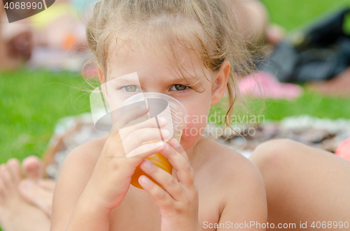 Image of The girl drinks juice from a plastic disposable cup on a picnic