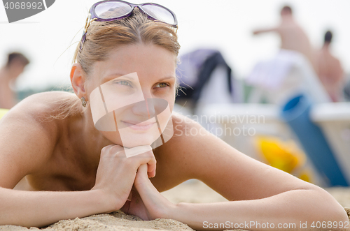 Image of Young girl lying on the sandy beach against the backdrop of other travelers and smiling looks into the distance