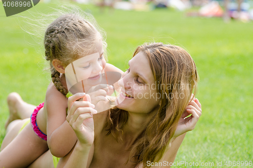 Image of Mom and daughter having fun lying on a green lawn in the summer