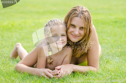 Image of Young mother and five year old daughter hugging lying on green grass and looking to the frame