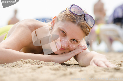 Image of Young girl lying on sandy beach and smiling looks into the frame