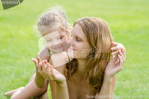 Image of Mom and daughter having fun embrace the summer picnic on a green lawn