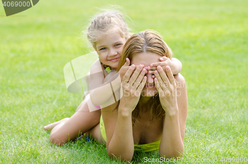 Image of The daughter of fun mom closed her eyes while lying on a green lawn