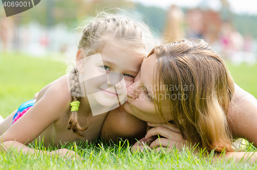 Image of Mother kissing her daughter lying on a green grass lawn