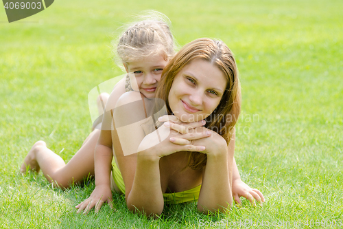 Image of Mum and daughter lie on a green lawn in a bikini and look in the frame