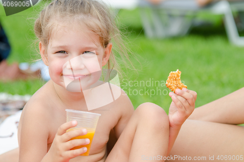 Image of Girl eats cookies, drinks juice from a plastic disposable cup and smiling looked into the frame