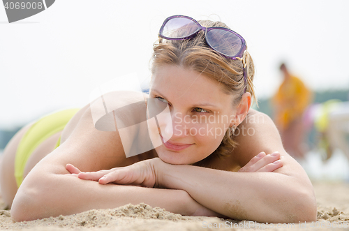 Image of Young girl lying on sandy beach and looking to the side