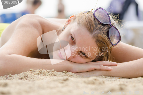 Image of Sad young girl lying on sandy beach and looking to the side