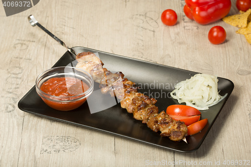 Image of shashlik. kebab skewer, black rectangular plate. sauce and onions