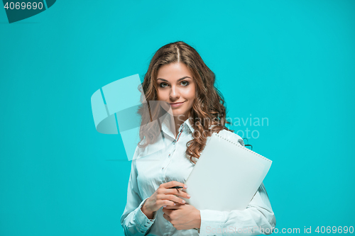 Image of The smiling young business woman with pen and tablet for notes on blue background