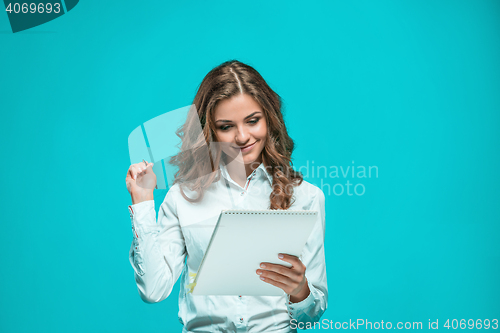 Image of The smiling young business woman with pen and tablet for notes on blue background