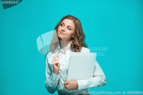 Image of The smiling young business woman with pen and tablet for notes on blue background