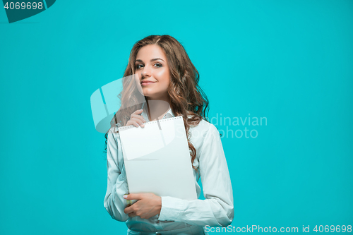 Image of The smiling young business woman with pen and tablet for notes on blue background